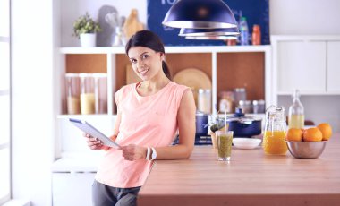 Mutfakta dijital tablet kullanan güzel genç bir kadın.