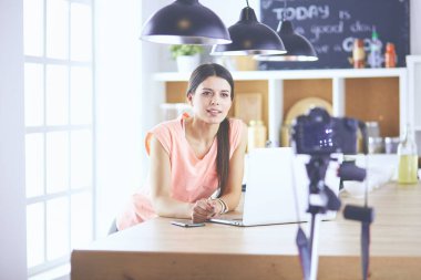 Mutfakta dizüstü bilgisayara benzeyen tariflerle gülümseyen genç bir kadın. Gıda blogcusu kavramı