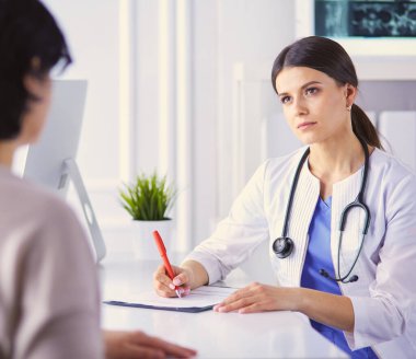 Doktor ve hasta hastane danışma odasında tıbbi sorunları tartışıyorlar. Doktor hasta formunu dolduruyor.