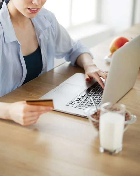 Χαμογελαστή γυναίκα online ψώνια χρησιμοποιώντας υπολογιστή και πιστωτική κάρτα στην κουζίνα — Φωτογραφία Αρχείου