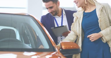 Kadın satıcısı galeride yeni bir arabanın yanında duruyor.