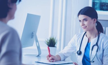Doktor ve hasta hastane danışma odasında tıbbi sorunları tartışıyorlar. Doktor hasta formunu dolduruyor.