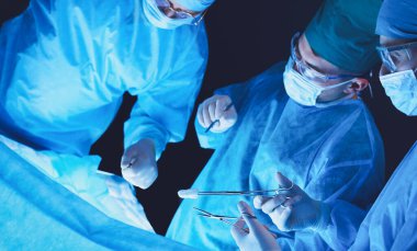 Ameliyathanede çalışan bir grup cerrah mavi tonda çalışıyor. Tıbbi ekip operasyon yapıyor.