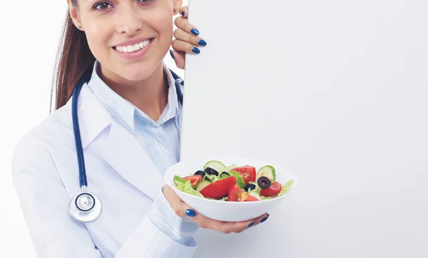 Portrait d'une belle femme médecin tenant une assiette avec des légumes frais debout près de blanc. Femmes médecins — Photo