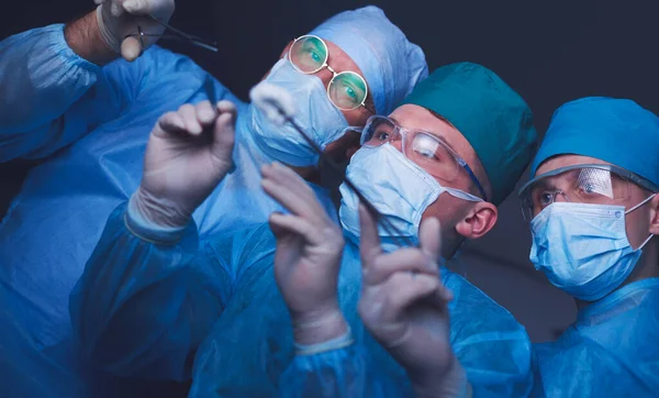 Grupo de cirurgiões no trabalho em sala de operações tonificada em azul. Equipe médica realizando operação — Fotografia de Stock