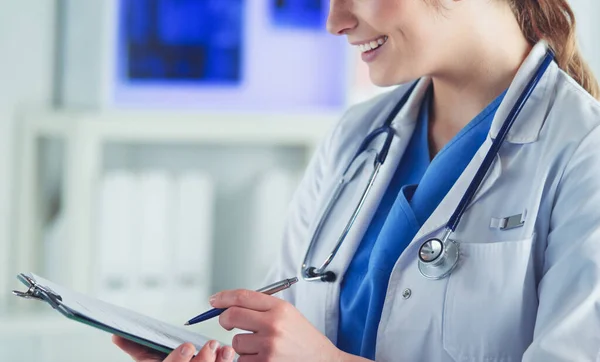 Doctor con un estetoscopio, sosteniendo un cuaderno en su mano. Primer plano de una doctora llenando el formulario médico en el portapapeles mientras está de pie en el hospital —  Fotos de Stock