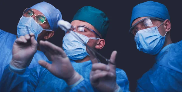 Grupo de cirurgiões no trabalho em sala de operações tonificada em azul. Equipe médica realizando operação — Fotografia de Stock