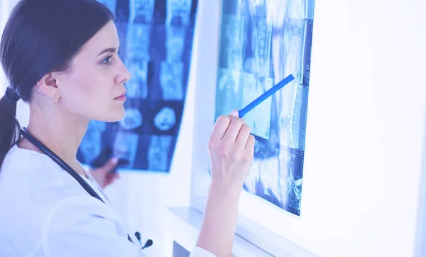 Молода усміхнена жінка-лікар зі стетоскопом, що вказує на рентген в кабінеті лікарів — стокове фото