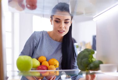 Gülümseyen kadın buzdolabından taze meyve alıyor, sağlıklı yiyecek konsepti.