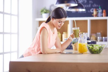 Mutfakta dijital tablet kullanan güzel genç bir kadın.