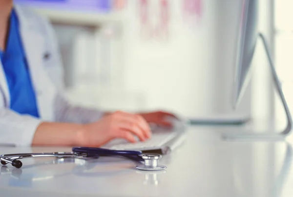 Nahaufnahme eines Stethoskops liegt auf dem Tisch neben Ärztin, die am Laptop tippt — Stockfoto