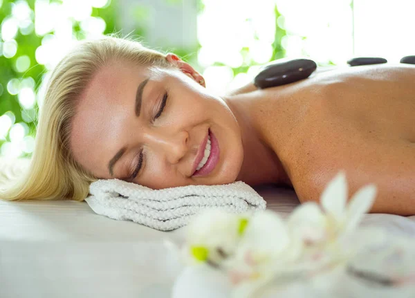 Beautiful young woman with eyes closed receiving hot stone massage at salon spa — Stock Photo, Image