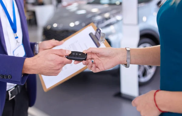 Car salesman sells a car to happy customer in car dealership and hands over the keys