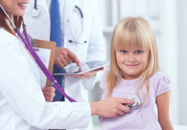 Kadın doktor ameliyatta steteskopla çocuğu muayene ediyor.