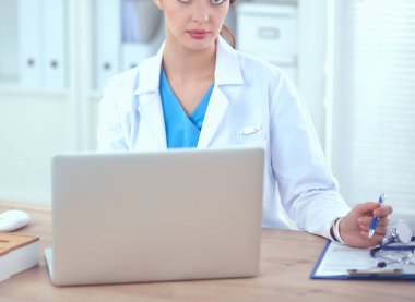 Güzel, genç, gülümseyen bayan doktor masada oturuyor ve yazıyor..