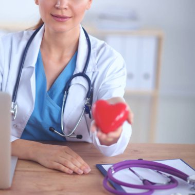 Kırmızı kalp sembollü genç doktor masasında tek başına oturuyor.