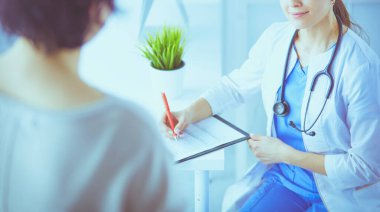 Doktor ve hasta hastane danışma odasında tıbbi sorunları tartışıyorlar. Doktor hasta formunu dolduruyor.