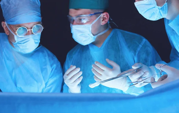 在手术室工作的一组外科医生用蓝色调.执行业务的医疗小组 — 图库照片