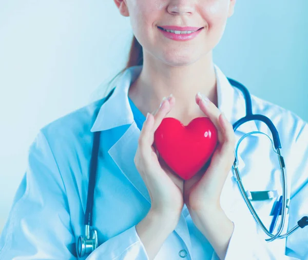 Bonito jovem sorridente médico feminino sentado na mesa e segurando o coração . — Fotografia de Stock