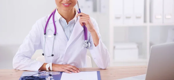 Bonito jovem sorridente médico feminino sentado na mesa e w — Fotografia de Stock