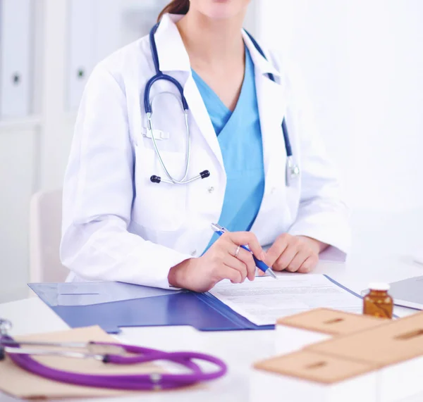 Bonito jovem sorridente médico feminino sentado na mesa e w — Fotografia de Stock