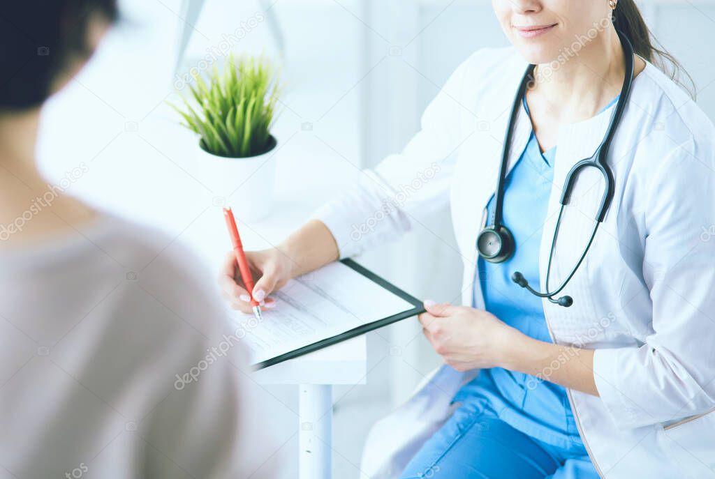 Doctor and patient discussing medical problems in a hospital consulting room. Doc filling in a patients form