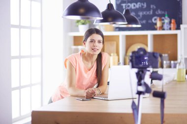 Mutfakta dizüstü bilgisayara benzeyen tariflerle gülümseyen genç bir kadın. Gıda blogcusu kavramı