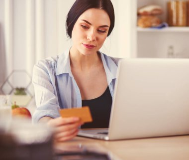 Mutfakta bilgisayar ve kredi kartı kullanan gülümseyen bir kadın.