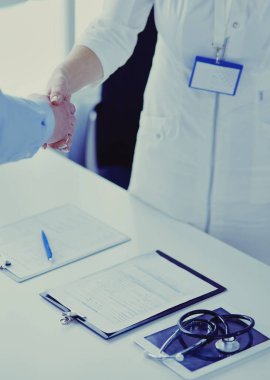 Kadın doktor bir hastanın elini sıkıyor ve gülümsüyor.