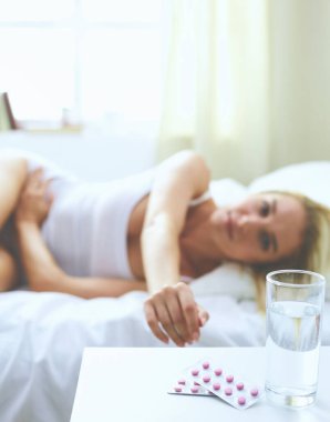 Genç, güzel bir kadın. Yatağında haplarla yatıyor.