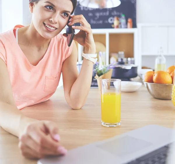 Νεαρή γυναίκα στην κουζίνα με φορητό υπολογιστή ψάχνει συνταγές, χαμογελώντας. Έννοια μπλόγκερ τροφίμων — Φωτογραφία Αρχείου