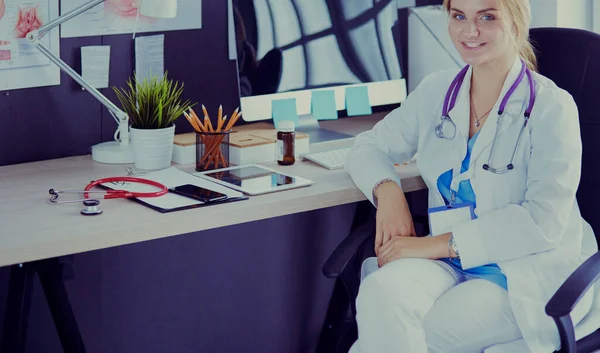 Krásná mladá usměvavá doktorka sedící za stolem — Stock fotografie