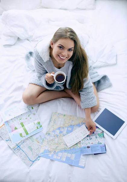 Relaxado jovem mulher sentada na cama com uma xícara de café e tablet digital — Fotografia de Stock