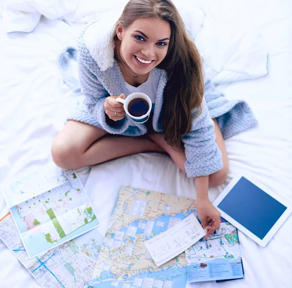 Mujer joven y relajada sentada en la cama con una taza de café y una tableta digital —  Fotos de Stock