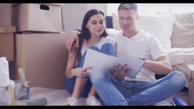 Genç ve çekici bir çift yerde oturan ve yeni evlerinin planına bakıp tasarımı düşünüyorlar. Kapalı