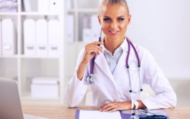 Güzel, genç, gülümseyen bayan doktor masada oturuyor ve yazıyor..