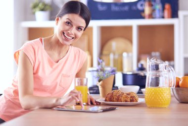 Mutfakta dijital tablet kullanan güzel genç bir kadın.
