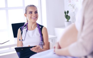 Steteskoplu ve tabletli genç kadın doktor hastanede hamile bir kadınla konuşuyor..