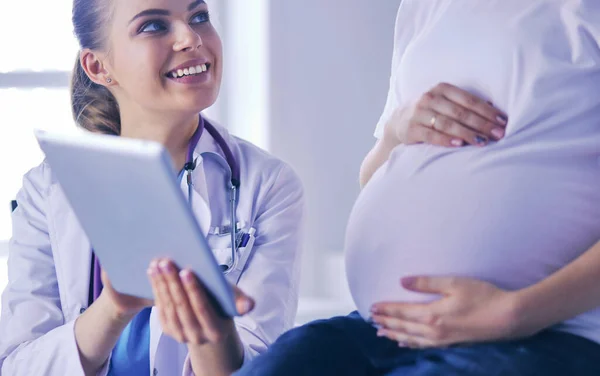 Leende kvinnlig läkare visar bilder på tabletten för gravida unga kvinnor på sjukhuset. — Stockfoto