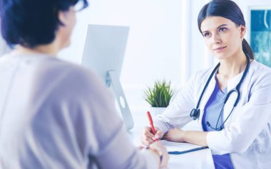 Doktor ve hasta hastane danışma odasında tıbbi sorunları tartışıyorlar. Doktor hasta formunu dolduruyor.