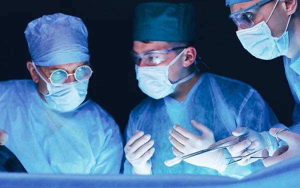 Grupo de cirurgiões no trabalho em sala de operações tonificada em azul. Equipe médica realizando operação — Fotografia de Stock