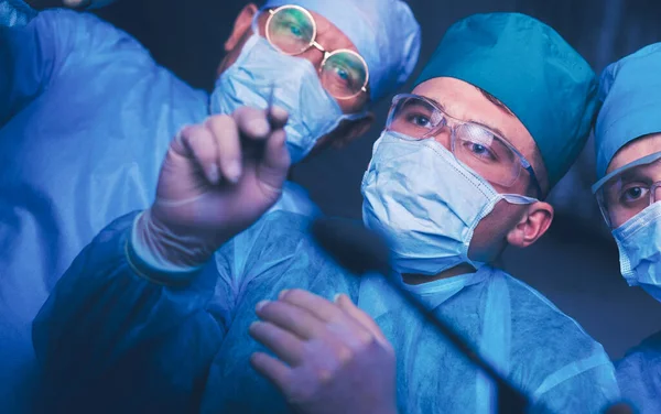 Grupo de cirurgiões no trabalho em sala de operações tonificada em azul. Equipe médica realizando operação — Fotografia de Stock