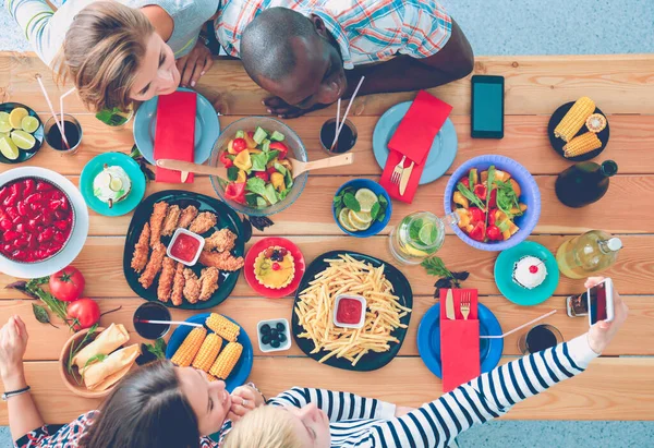 Top view of group of people having dinner together while sitting at wooden table. Food on the table. People eat fast food. — Stock Photo, Image