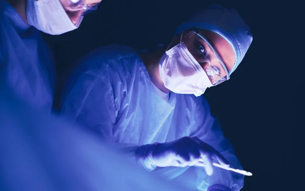 Equipo de médicos en cirugía en un fondo oscuro. — Foto de Stock