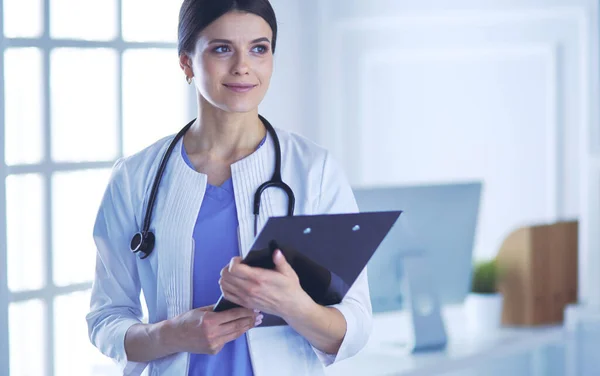 Jeune femme médecin souriante avec stéthoscope tenant un dossier au cabinet des médecins — Photo