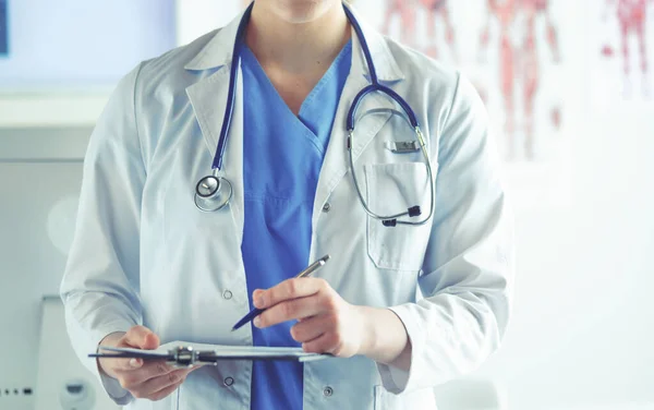 Doutor com um estetoscópio, segurando um caderno na mão. Close-up de um médico do sexo feminino preenchendo formulário médico na área de transferência, enquanto em pé em linha reta no hospital — Fotografia de Stock