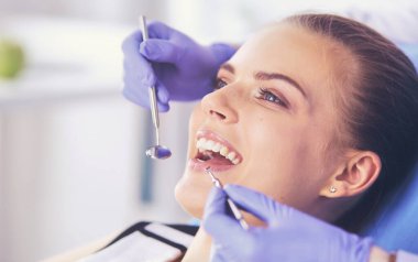 Dişçi muayenehanesinde diş muayenesi yapan ağzı açık genç bir kadın hasta..