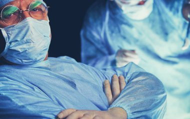 Ameliyathanede çalışan bir grup cerrah mavi tonda çalışıyor. Tıbbi ekip operasyon yapıyor.