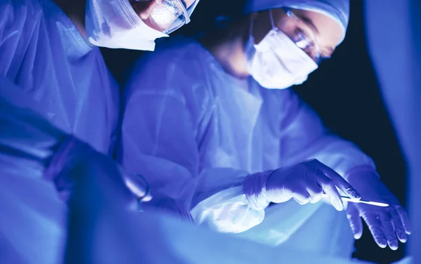 Ärzteteam in der Chirurgie vor dunklem Hintergrund. — Stockfoto