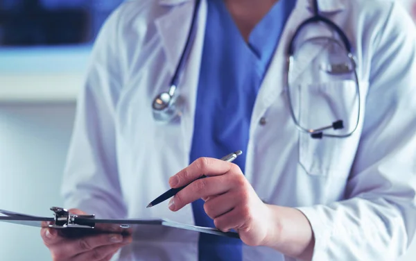 Doctor con un estetoscopio, sosteniendo un cuaderno en su mano. Primer plano de una doctora llenando el formulario médico en el portapapeles mientras está de pie en el hospital —  Fotos de Stock